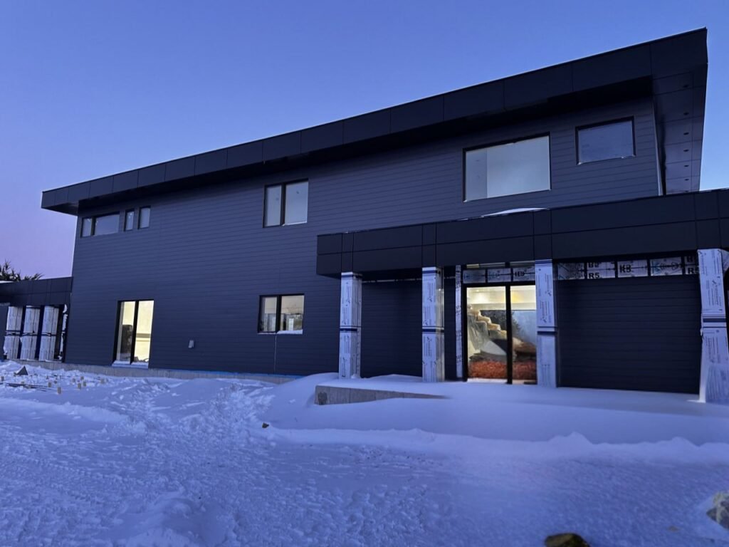 Modern two-story building featuring horizontal dark gray aluminum siding installation during winter at twilight.