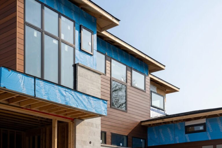 Modern residential home exterior under construction showcasing blue weather resistant barrier and newly installed horizontal woodgrain aluminum siding